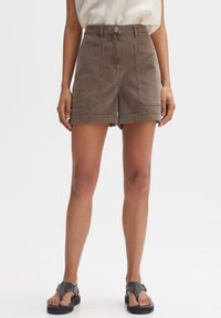 Bruine hoge taille shorts met twee voorzakken en opgerolde mouwen, gemaakt van zachte katoenstof. Gecombineerd met zwarte sandalen.