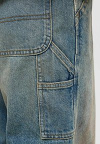 Denimske kratke hlače s svetle modre pranja, šivi so strojno obdelani, na strani pa je všit žep. Tkanina ima teksturiran, nekoliko zbledel videz.