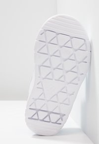 Vit atletisk skosula med en texturerad gummiyta som har ett diamantmönster och ett präglat logotyp. Ren design med minimala accenter.