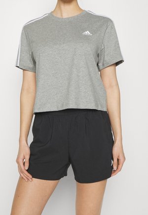 Personne portant un t-shirt court gris Adidas avec des bandes blanches sur les manches et un short de sport noir à taille élastique.