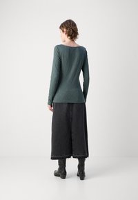 Ilga rankovė, tamsiai žalia palaidinė su apvaliu iškirpimu; derinama su ilga juoda džinsine sijonu su žaliuotu apvadu ir subtiliais nutrinimais, dėvima su juodais batais.