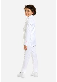 Giacca bianca con un solo bottone, pantaloni bianchi coordinati e sneakers bianche. Il tessuto appare liscio con una vestibilità su misura.