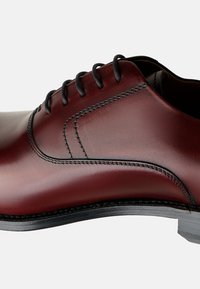 Scarpa da uomo in pelle marrone con finitura liscia, lacci neri e cuciture a contrasto. Presenta una punta arrotondata e una suola resistente.