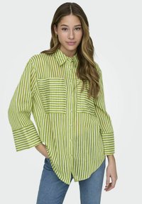 Camisa de botón a rayas verdes con cuello, dos bolsillos en el pecho y mangas anchas, hecha de un tejido ligero. Presenta rayas alternas de color claro y oscuro.