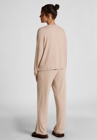Beige loungewear set bestaande uit een losvallende trui en bijpassende broek. Zachte textuur, ruime mouwen en een relaxte silhouette.