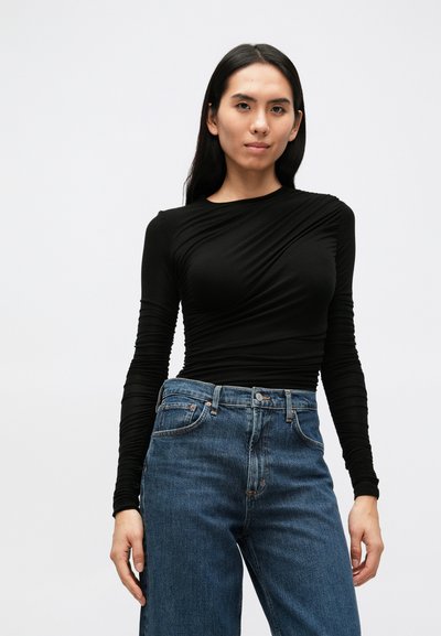 Črna majica z dolgimi rokavi z teksturiranim, padajočim dizajnom, kombinirana z visokim pasom modrih denim hlač. Gladek material in oprijet kroj.