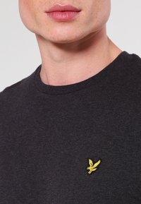 Czarny bawełniany t-shirt z okrągłym dekoltem, z małym, haftowanym żółtym logo orła po lewej stronie klatki piersiowej.