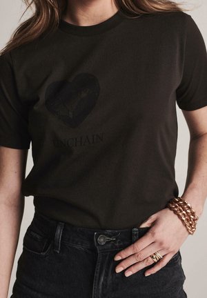 Czarny bawełniany t-shirt z krótkimi rękawami, na którym znajduje się grafika ciemnego serca oraz nadruk z napisem „UNCHAIN” poniżej. W połączeniu z ciemnymi dżinsami.