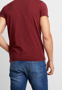 Camiseta de manga corta color burdeos con escote redondo, combinada con vaqueros azules con bolsillos traseros y detalles de costuras.