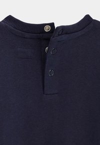 Tissu bleu marine en gros plan montrant un col de chemise avec trois boutons-pression partiellement défaits.