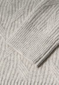 Tissu de pull gris clair avec un motif côtelé texturé et une finition lisse, avec une manche pliée affichant un design similaire.