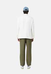 Witte getailleerde blazer met gouden knopen, gecombineerd met olijfgroene wijde broek en witte sneakers, afgewerkt met een lichtblauwe pet.