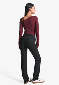 Burgundska dolga majica z odprtimi rameni, v kombinaciji z črnimi naravnost krojenimi jeans hlačami in belimi supergami z rjavimi detajli.