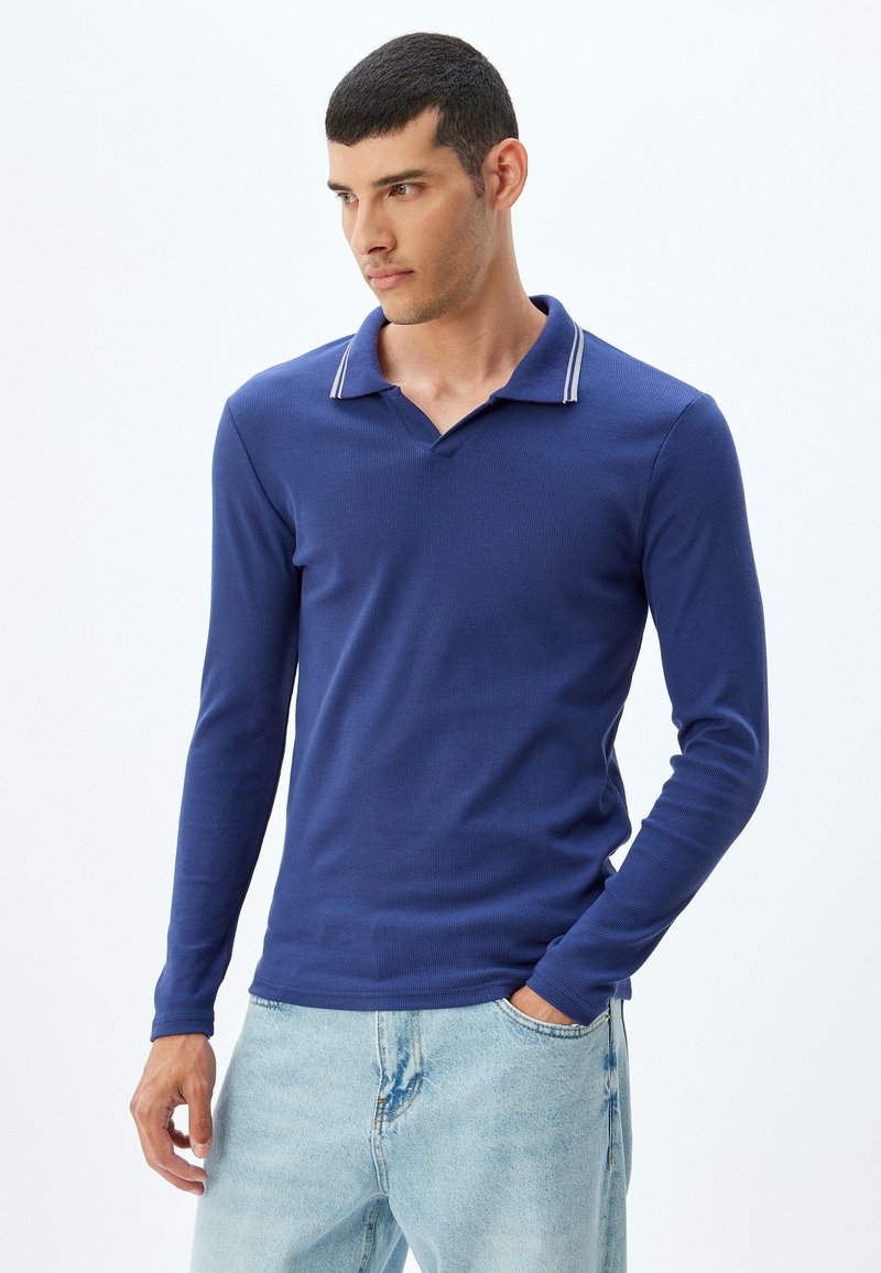 Marinblå långärmad polo med ribbad textur, kontrasterande randig krage och en avslappnad passform. Bärs med ljusblå jeans.