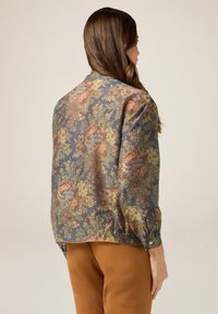 Blommig blus i texturerat tyg med en mörkblå bakgrund och flerfärgade blommor, långa puffärmar och en knappslutning vid ärmen.