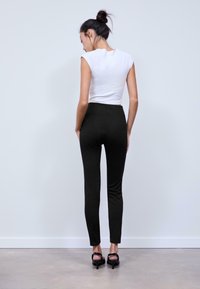 Pantaloni neri aderenti con vita alta e gamba slim, abbinati a una maglietta bianca a maniche corte. La modella indossa dei tacchi aperti neri.