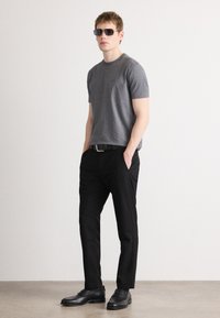 Γκρι κοντομάνικο μπλουζάκι, μαύρο παντελόνι και μαύρα παπούτσια. Σλιμ fit σχέδιο με μια διακριτική λογότυπο στο στήθος και ορθογώνια γυαλιά ηλίου.