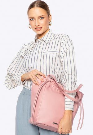 Borsa in pelle rosa con coulisse, dalla texture liscia e con spallacci lunghi, tenuta da una persona con una camicia a righe con dettaglio di balze.