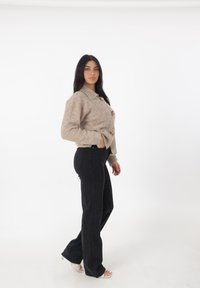 Giacca corta beige e pelosa con tre bottoni rotondi, abbinata a jeans neri svasati e sandali con tacco trasparente. Design semplice e moderno.