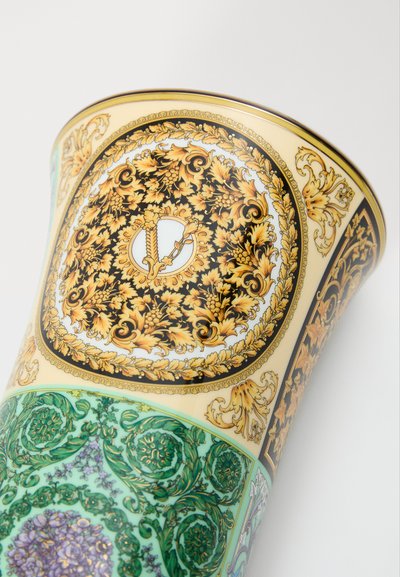 Vaso de cerâmica com padrões florais intrincados em dourado e preto, detalhes em verde e forma afunilada com borda decorativa.