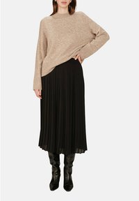 Pull en tricot beige à coupe décontractée, associé à une jupe midi plissée noire et des bottes noires montantes, mettant en valeur la texture et les superpositions.