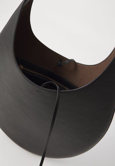 Melnas ādas rokassomiņa ar gludu tekstūru, izliekta dizaina un brūnu interjeru. Ietver rāvējslēdzēja kabatu un plānu melnu jostu.