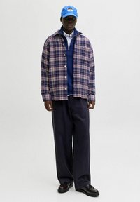 Camicia a quadri in blu navy, rosa e bianco; sovrapposta a un maglione blu navy e a una camicia bianca; abbinata a pantaloni larghi scuri e scarpe nere.