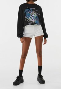 Camisa negra de manga larga con gráficos coloridos; combinada con pantalones cortos de mezclilla blancos y zapatillas de plataforma negras con calcetines negros.