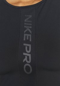 Haut sportif noir avec le texte "NIKE PRO" en gris réfléchissant sur le devant. Confectionné en tissu lisse et extensible avec un col rond.