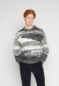 Maglione a maglia nero e bianco con scollo rotondo e maniche lunghe. I polsini e l'orlo a costine forniscono texture e calore.