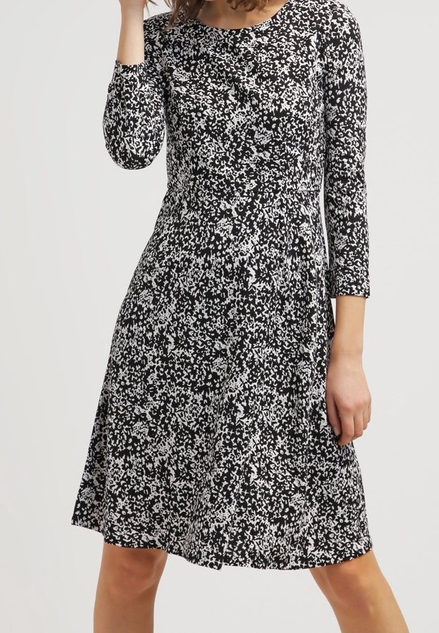 Femme portant une robe mi-longue noire et blanche à motifs, manches trois-quarts et col rond.