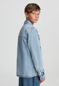 Jasnoniebieska kurtka dżinsowa o klasycznym kroju, z zapięciem na guziki przy mankietach i kieszenią na piersi. Charakteryzuje się wyraźnym przeszyciem oraz lekkim wyblaknięciem dla uzyskania tekstury.