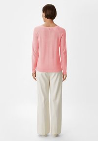 Helles rosa Sweatshirt mit langen Ärmeln und geripptem Stoff, ausgestattet mit einem Rundhalsausschnitt und einer Knopfdetails auf der Rückseite, kombiniert mit cremefarbener Hose.