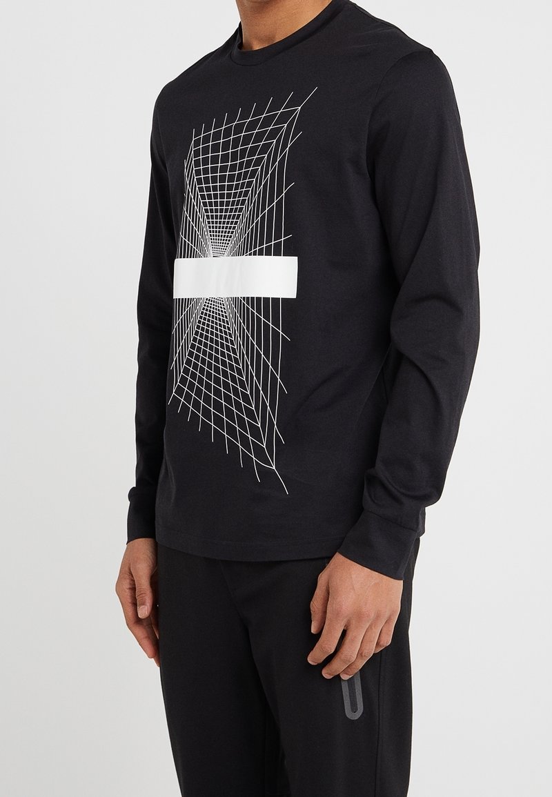 Svart långärmad skjorta med en vit geometrisk rutdesign på framsidan och ett solidt vitt horisontellt band över mitten.