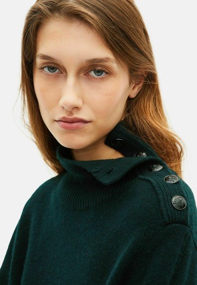 Maglione verde scuro con colletto alto e bottoni neri sulla spalla. Il tessuto ha un aspetto morbido e texturizzato.