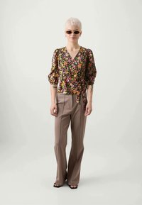 Blus med blommönster och puffärmar, V-ringning och knytdetalj, kombinerad med högmidjade beige byxor med ränder och utsvängda ben.