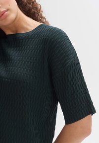 Haut vert foncé texturé avec un design côtelé, des manches courtes et un col rond, confectionné dans un tissu doux et extensible.
