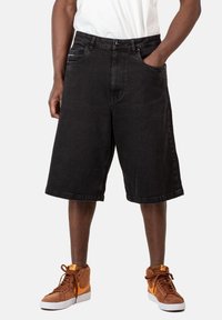 Shorts de mezclilla negra con un ajuste relajado, que cuentan con bolsillos laterales, dobladillo recto y detalles de costura sutiles, combinados con zapatillas altas marrones.