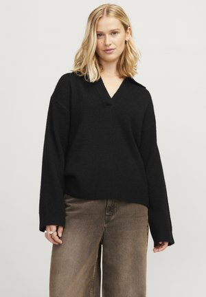 Maglione nero, oversize, con scollatura a V, maniche lunghe e una texture morbida. Abbinato a jeans marroni a vita alta. Design minimalista.