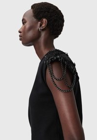 Czarna sukienka z teksturowanymi ozdobami na ramionach z detalem łańcuszka. Tkanina wydaje się gładka, a akcenty na ramionach są warstwowe.