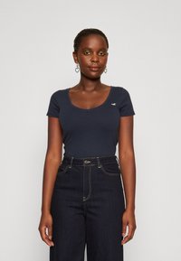 Top corto de color azul oscuro con escote redondeado, hecho de una tela suave. Combinado con jeans de mezclilla oscuros de cintura alta con costuras en contraste.