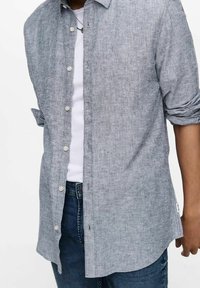 Camisa gris de botones hecha de tejido texturizado, con cuello clásico, mangas largas con puños enrollados y dobladillo curvado.