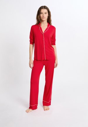 Rød pyjamas sæt med en knap-op top med hvid piping, lange ærmer og matchende bukser med en løs pasform og hvid kant ved anklerne.