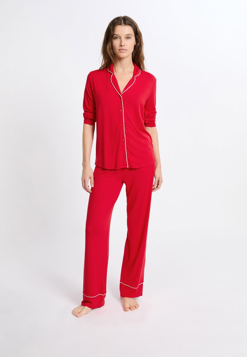 Czerwony zestaw piżamowy z guzikowym topem z białym wykończeniem, długimi rękawami oraz dopasowanymi spodniami o luźnym kroju z białymi lamówkami przy kostkach.