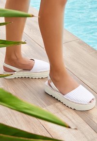 Sandalias blancas tipo slingback con parte superior texturizada y suela de plataforma. Presentan un patrón tejido y una suela de goma en contraste.