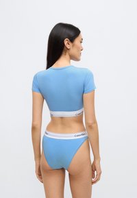 Μπλε βαμβακερό crop top με κοντά μανίκια και λευκή ελαστική ζώνη μέσης με τη σήμανση "Calvin Klein", συνδυασμένο με αντίστοιχο εσώρουχο.