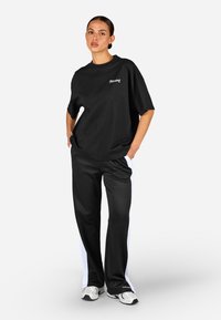 Czarny, oversize t-shirt z białym logo, w połączeniu z czarnymi spodniami elastycznymi w pasie z białymi paskami po bokach. Wygodny materiał i casualowy design.