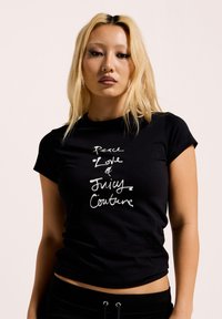 Zwarte slimfit t-shirt met korte mouwen, voorzien van handgeschreven witte tekst: "Peace Love & Juicy Couture." Glad weefsel, ronde hals.