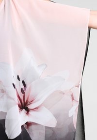 Tessuto rosa pallido con grande stampa di fiori di giglio bianchi e rosa, tenuto aperto per mostrare la trama trasparente e il design delicato.