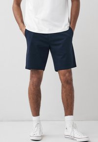 Pantalones cortos azul marino de tela suave, con un corte recto y bolsillos laterales, combinados con zapatillas altas blancas y calcetines de longitud media.
